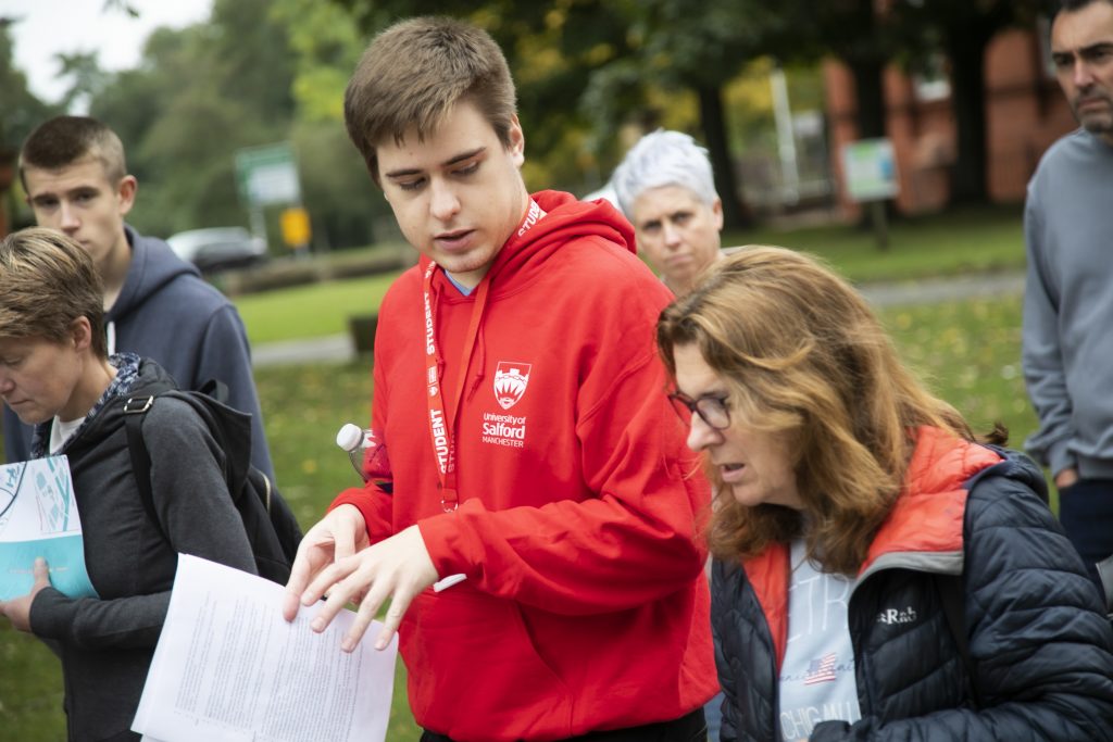 Photo of a volunteer wearing salford uni red hoodie guiding people