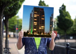 Man holding large photograph of a buidling in front of his face.