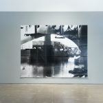 Black and white photograph of water and an industrial building in the distance.