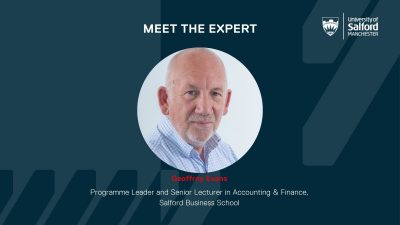 Geoffrey Evans smiling towards the camera in the middle of a dark blue background.