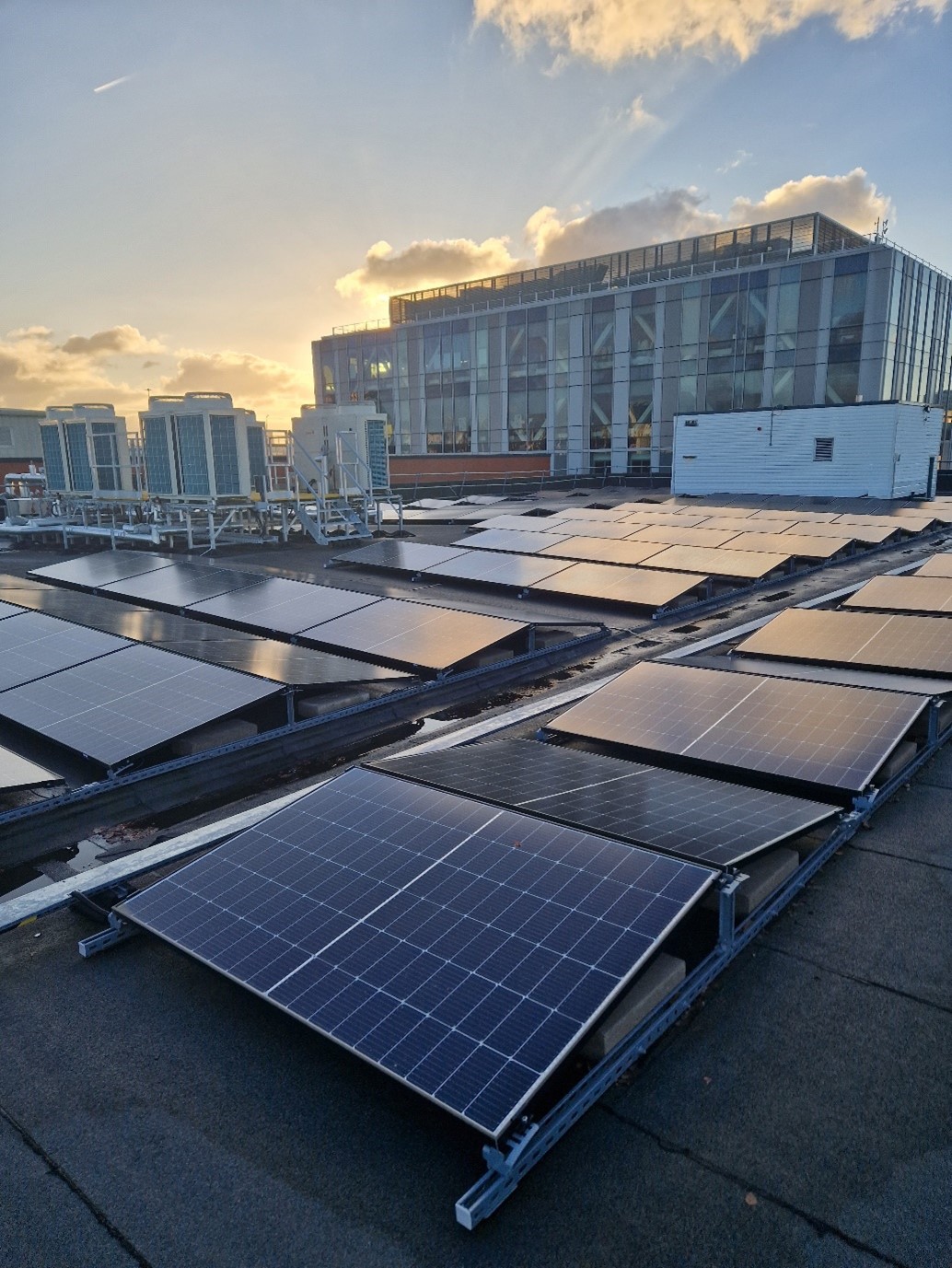 A roof top view of solar panels and air source heat pumps at sunset