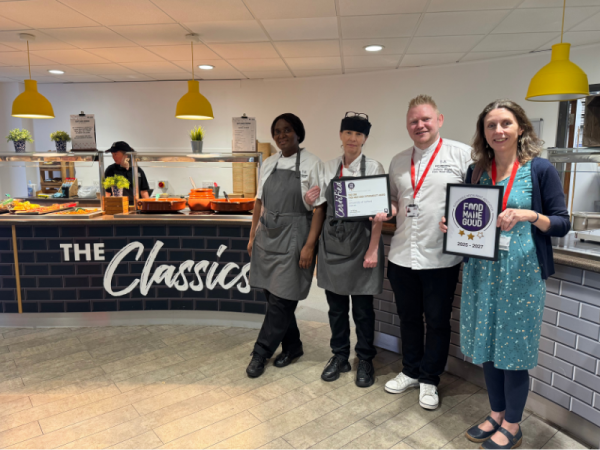 A group of people stood in a canteen holding two certificates