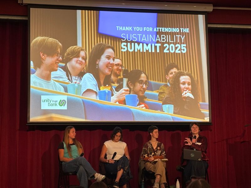 Four people sat on a stage with a screen above them that says "Thank you for attending the Sustainability Summit 2025"