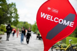 A Welcome banner in the Peel Park campus with some students walking in the background.