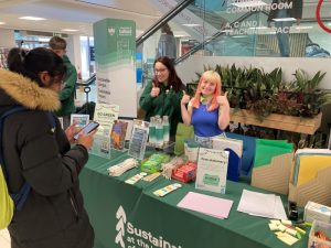 Sustainability Team members smiling and holding their thumbs up stood behind their promotional stall.