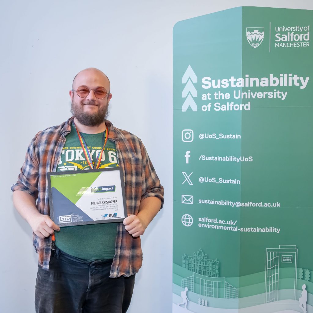 A person stands between two green sustainability banners holding a framed certificate and smiling.