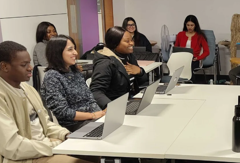 Students sat at a table smiling with laptops.
