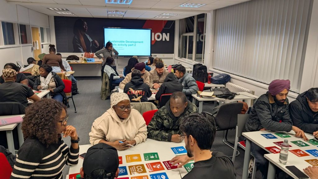 People sat around tables of 4 people, working together with cut-out icons of the 17 Sustainable Development Goals.