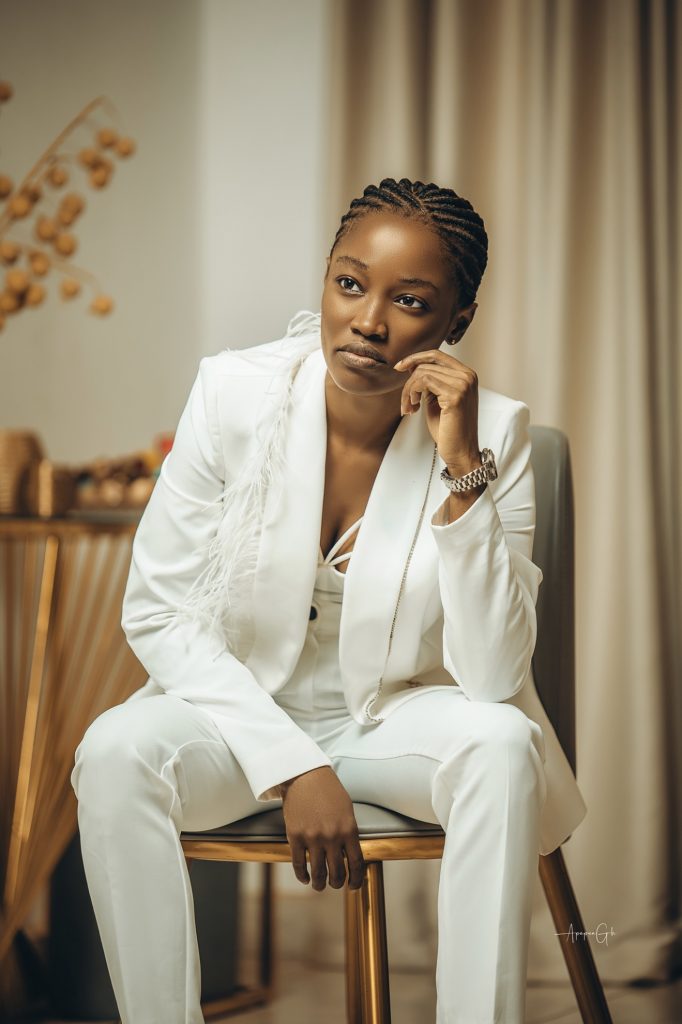 Deborah sat on a chair wearing a ehite suit and a watch.