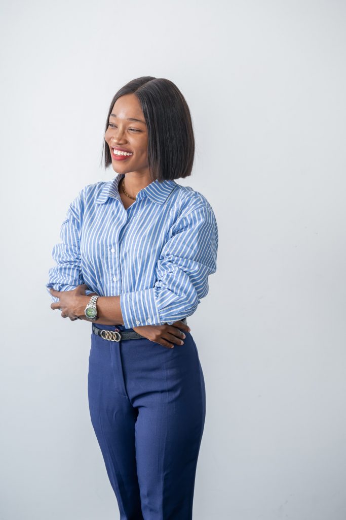 Deborah stood smiling, wearing navy jeans, a blue and white stripy shirt, a belt and a watch.