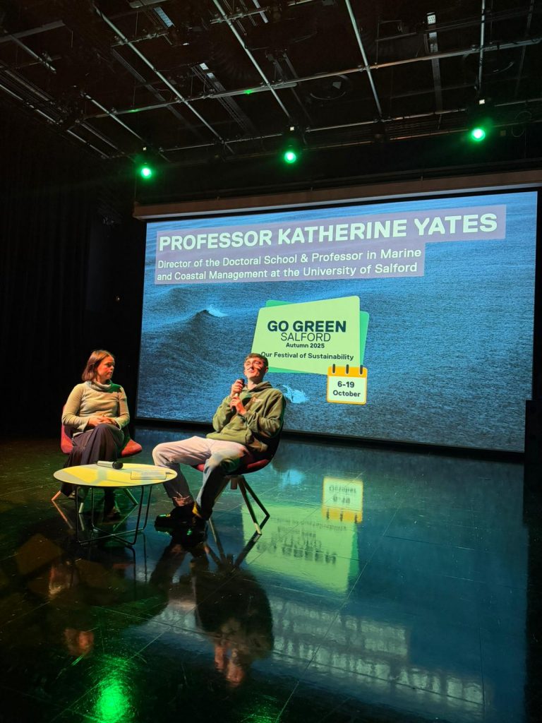 Two people sat with microphones on a stage.