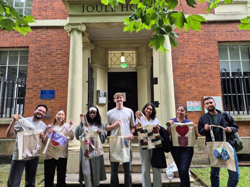People stood on campus holding tote bags smiling.