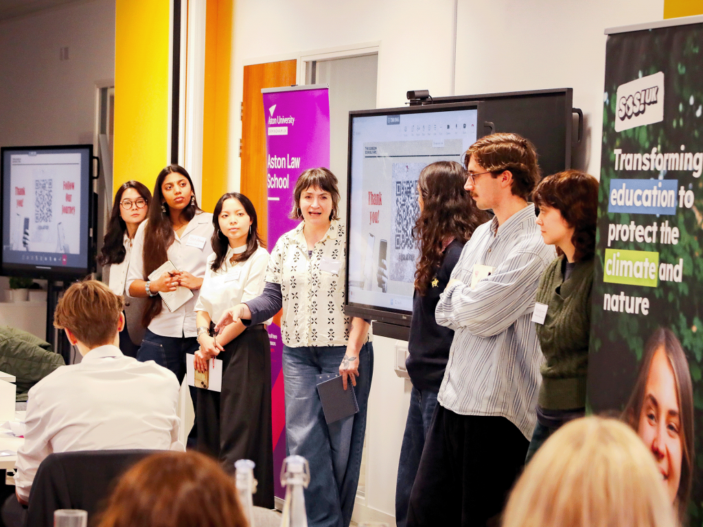 Participants presenting at a university sustainability event, standing beside display screens and banners while addressing an audience.