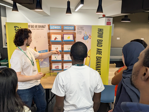 Picture of someone pointing to the activity in front of them called How Bad are Banana's with a group of people tentatively looking at what they are talking about.
