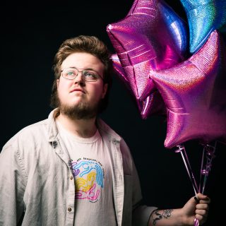 Ben Hodge holding a display of pink and blue balloons, the colours of the Trans flag