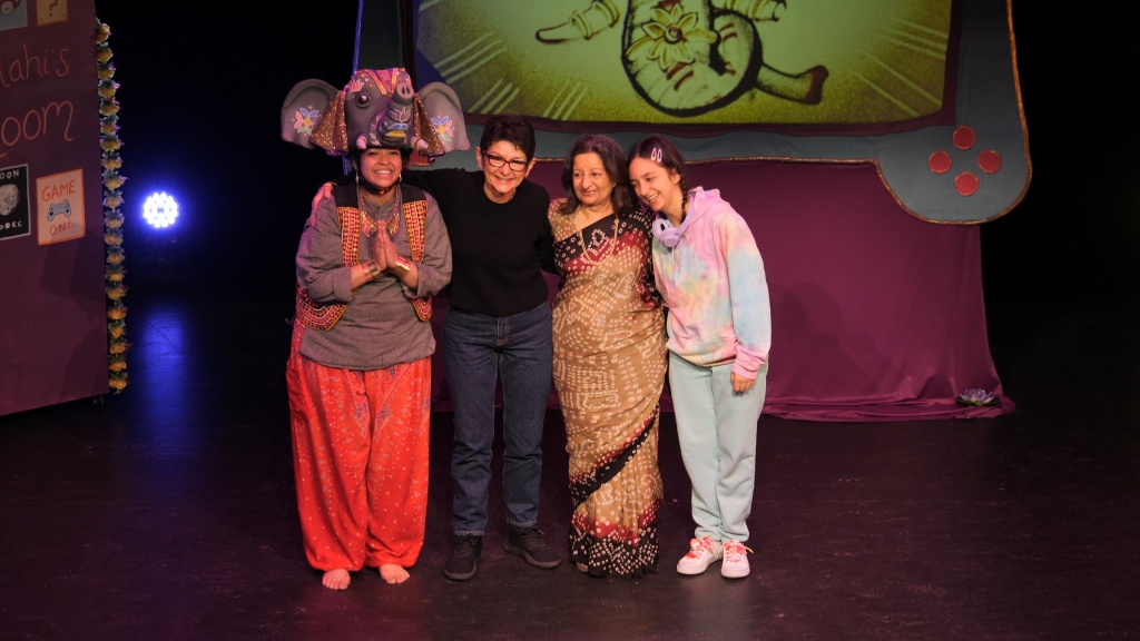 This image shows 4 cast members from the dancing elephant. One is wearing an elephant's mask, another is dressed in a black jumper and trousers, another is in traditional asian dress, while the final is wearing casual comfortable clothes.