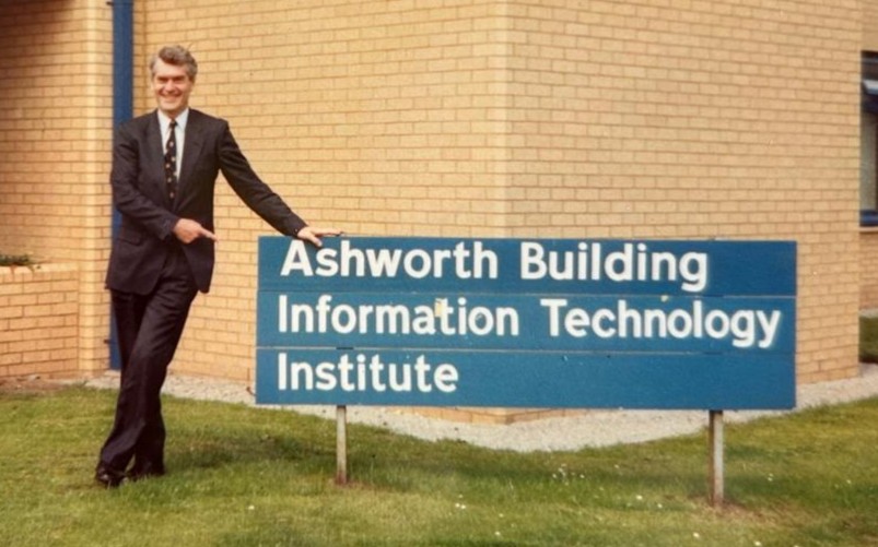 Sir John Ashworth leaning against the sign at Ashworth Building in 1991