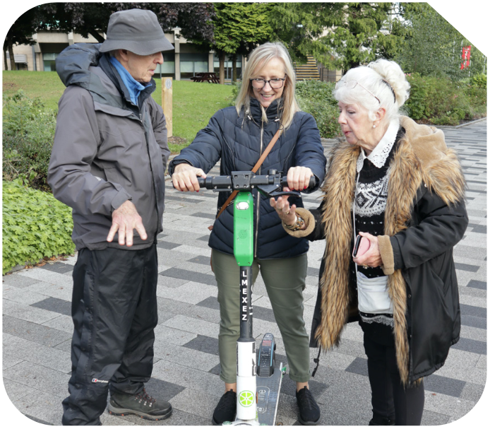 Three older age white people are looking at a lime e-scooter and laughing
