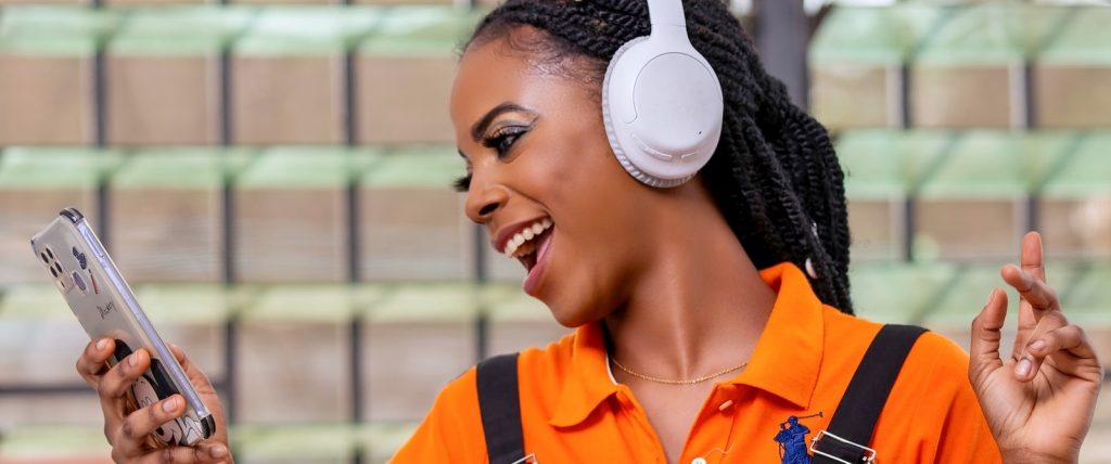 Photograph of a young woman wearing headphones, and singing along to music on her smart phone.