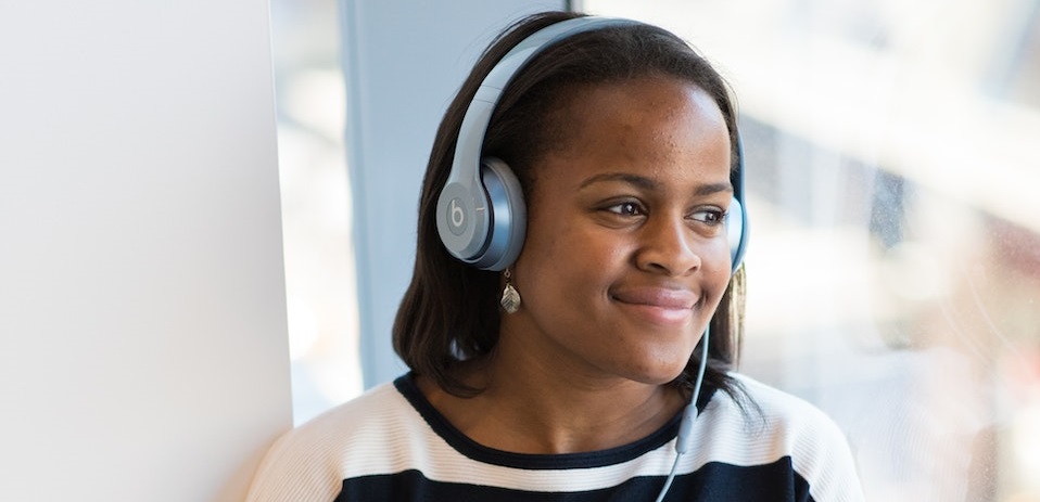 Smiling girl in striped jumper, listening to audio on her headphones.
