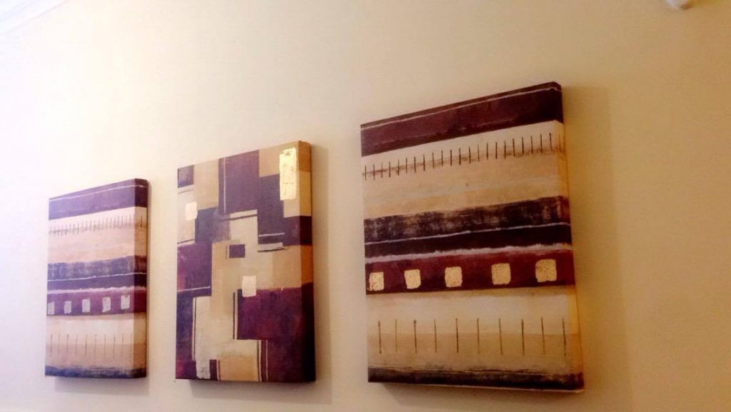 3 abstract art works on a wall all with red, gold and orange colours.