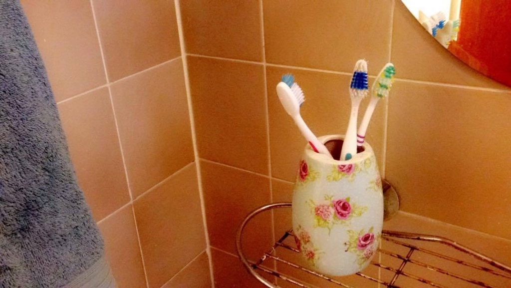 3 toothbrushes in a pot on a shelf in a bathroom