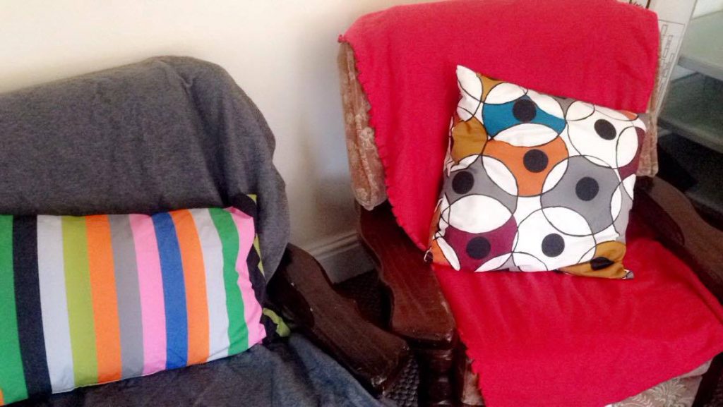 2 light red armchairs with wooden legs and arms with different colour throws over them