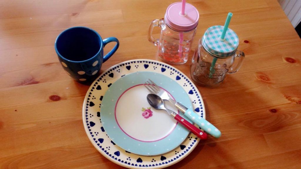 a mug, plate and 2 glasses with straws on a table