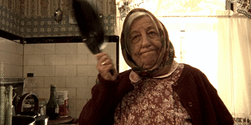 Old woman with a head scarf hitting her head with a frying pan