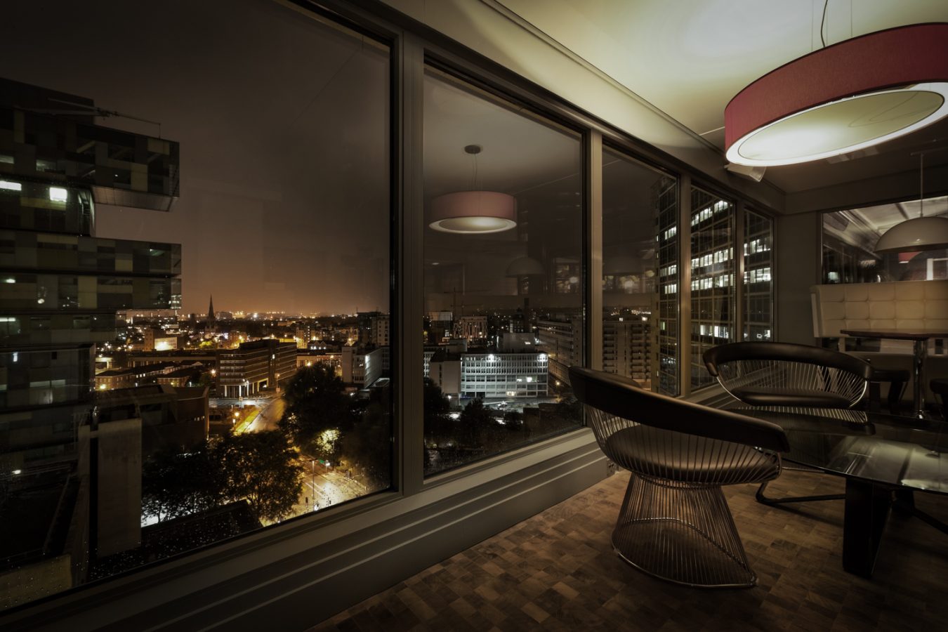 A view of inside the bar with some seating next to a window that overlooks a view of the city at night time