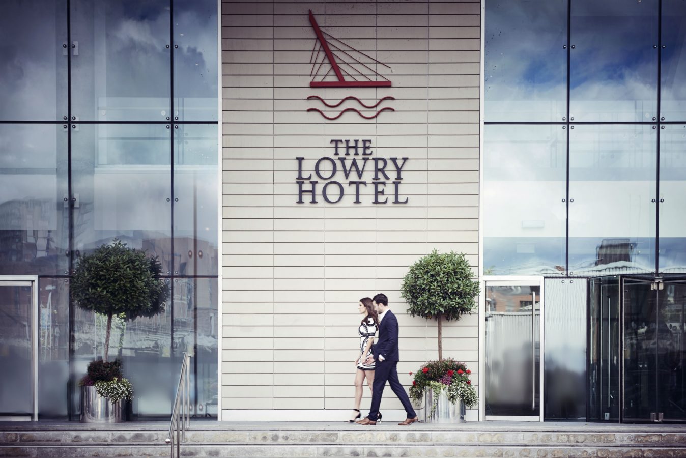 A man and a woman walking in front of the Lowry Hotel exterior with the hotels sign on a wall above them