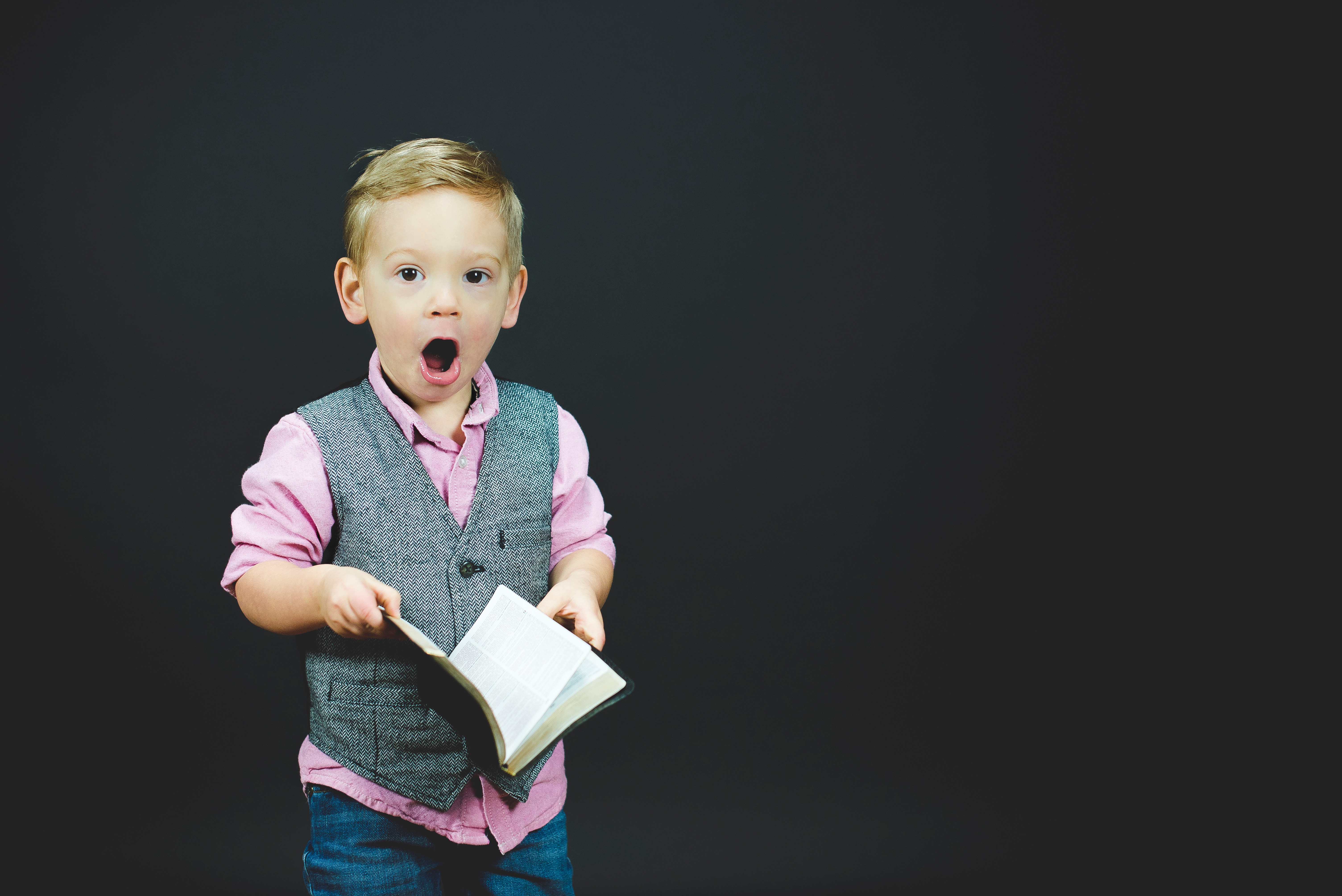 A little boy against a black background holding a book