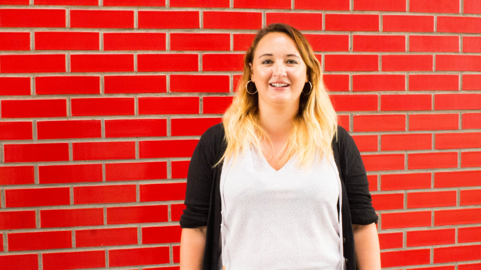 Eve stood next to a red brick wall looking towards the camera