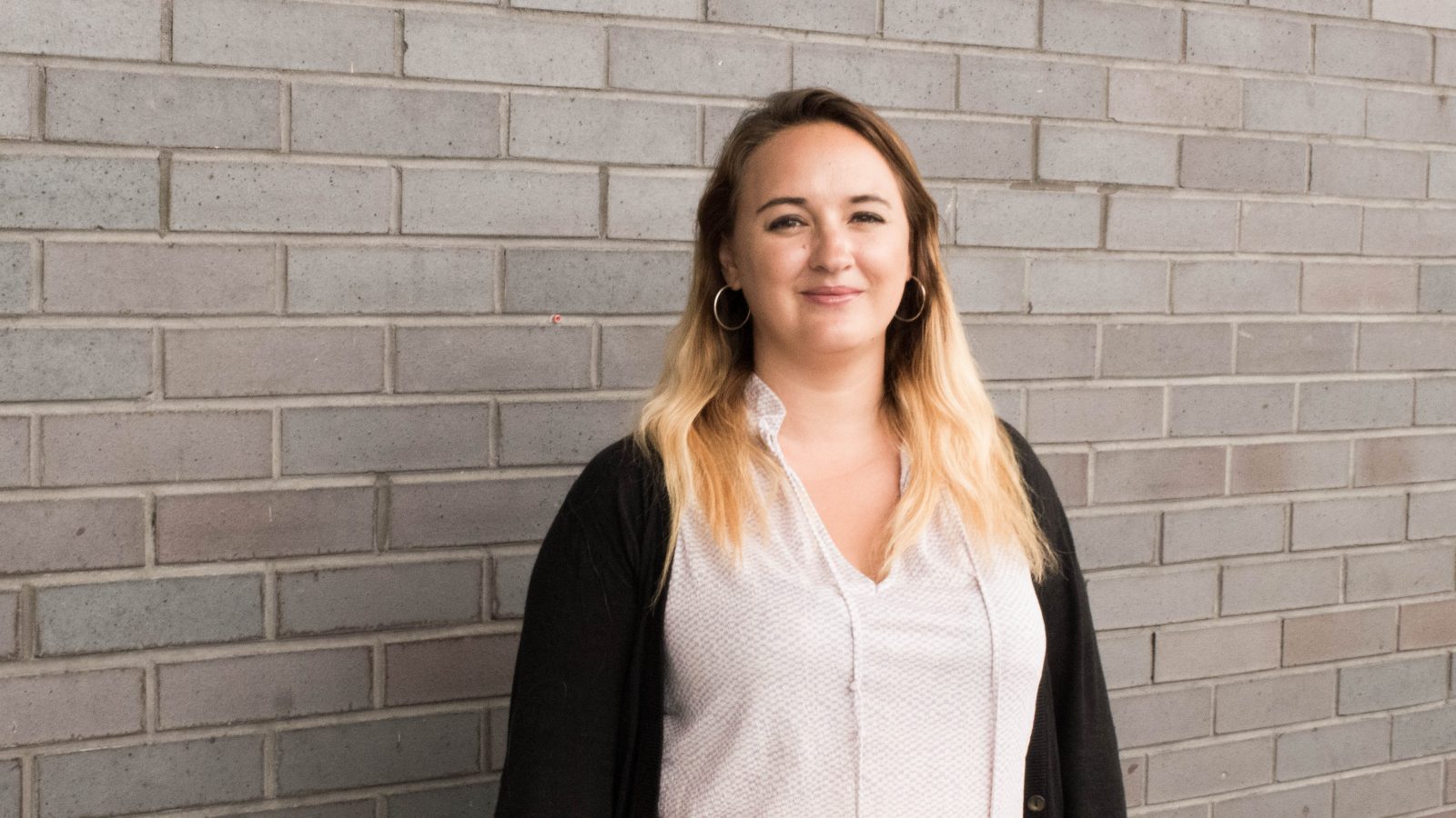 Eve stood next to a dark brick wall looking towards the camera