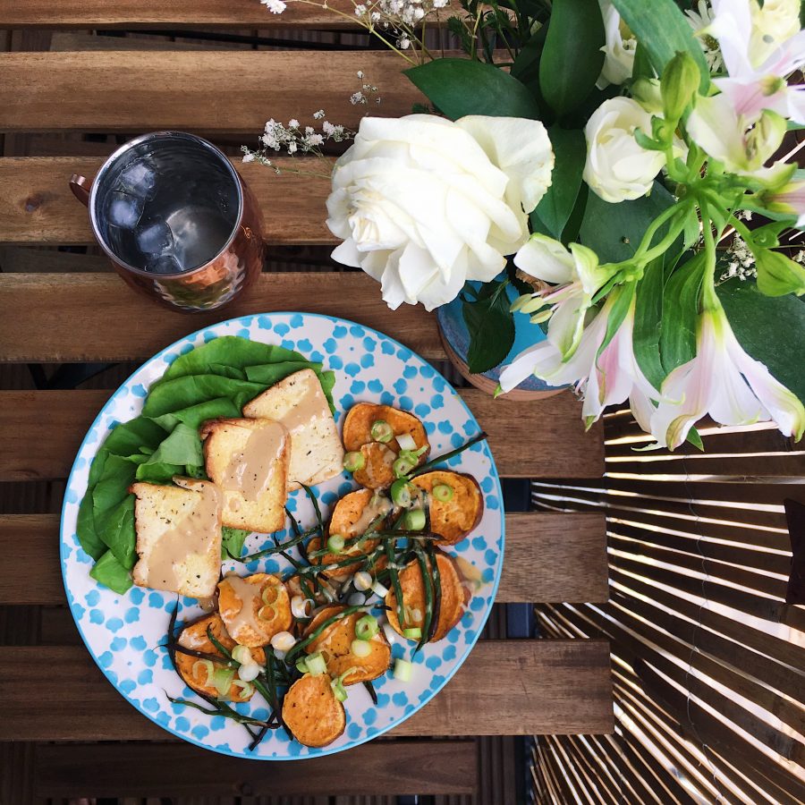 Tahini drizzled over tofu and sweat potato on a blue plate