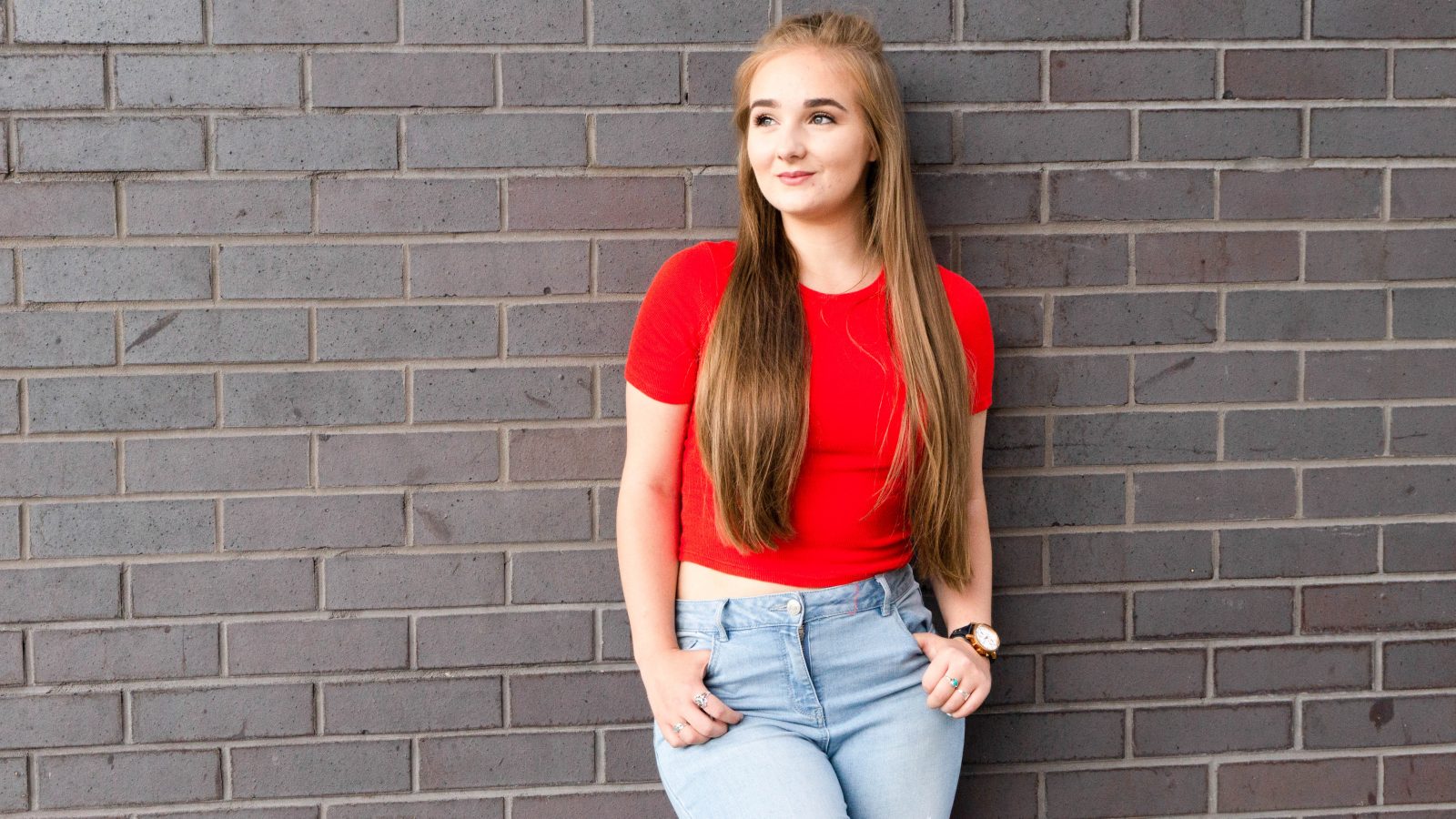 Becky stood next to a dark brick wall with her hands in her pockets