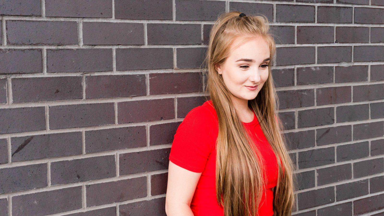 Becky leaning against a dark brick wall facing down