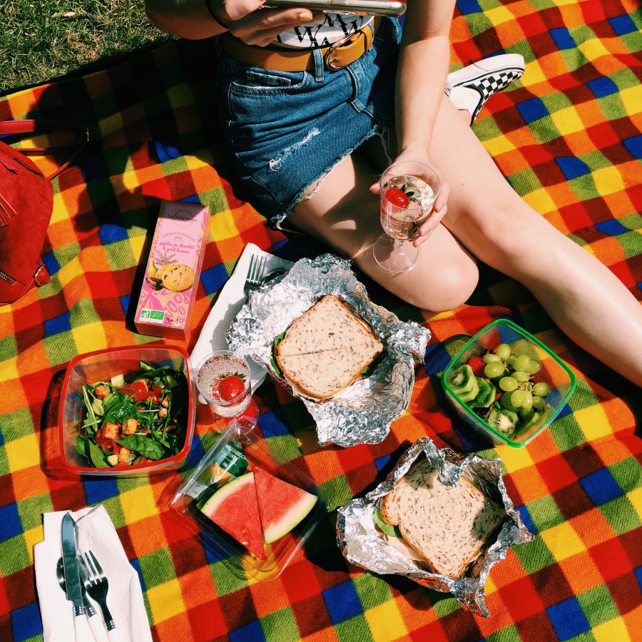 Someone sat on a multicoloured chequered blanket having a vegan picnic
