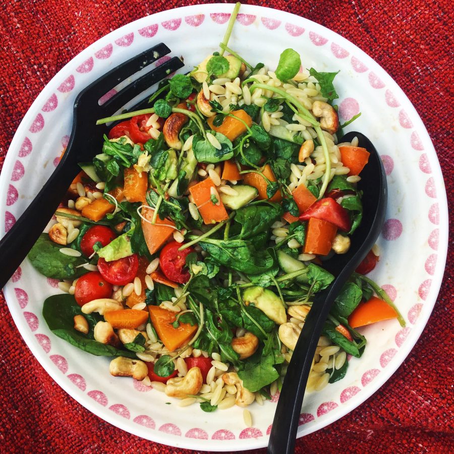 Orzo salad in a white bowl on a table with a red tablecloth
