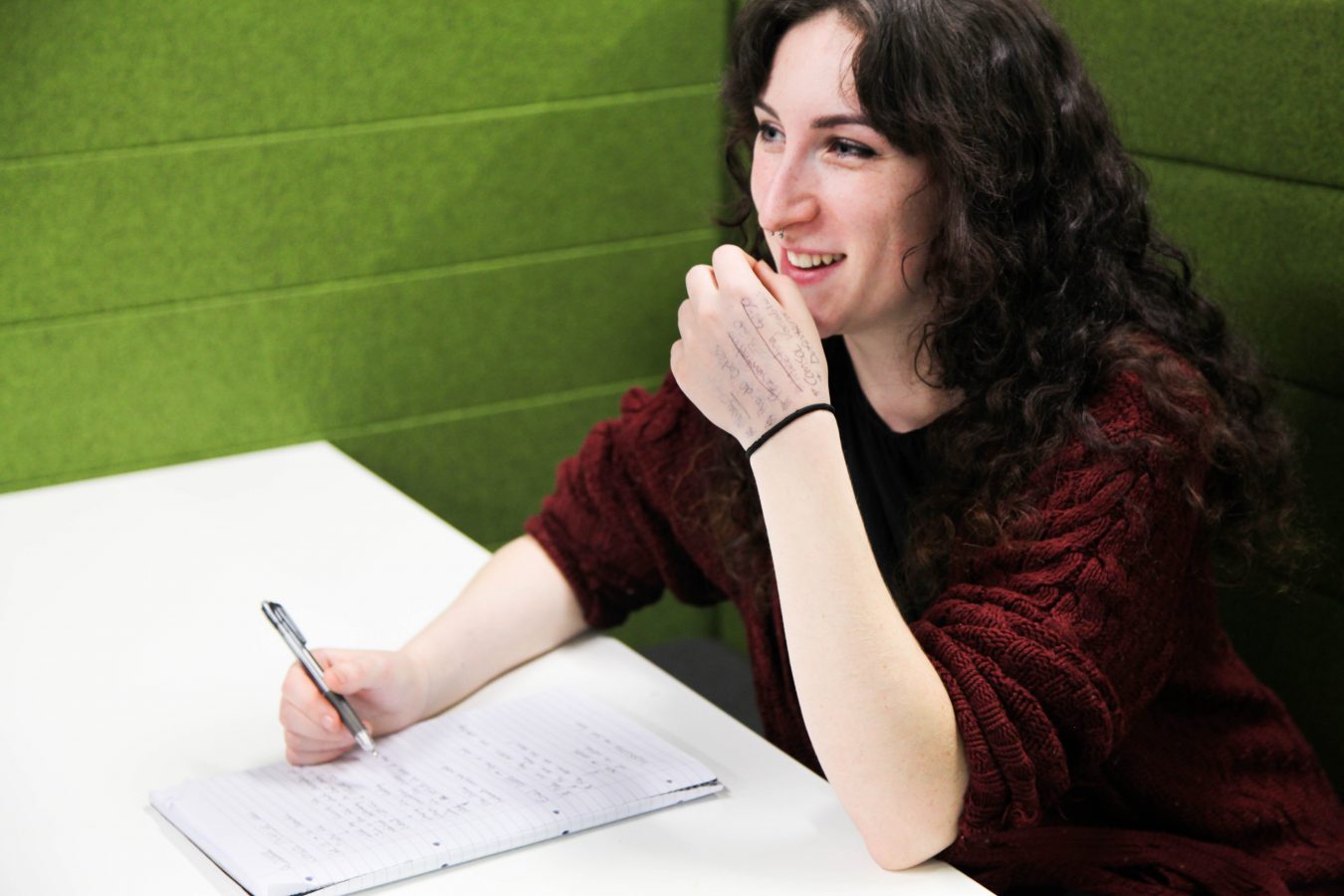 Elle Kalavsky smiling whilst writing at table.