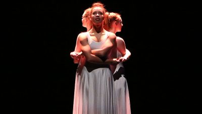 Three University of Salford students in white dresses performing on stage
