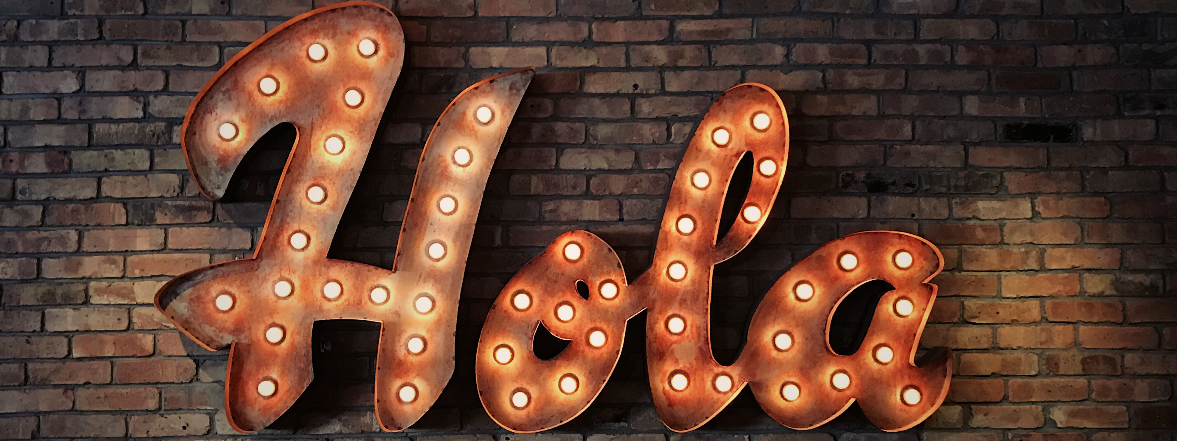 the word 'Hola' in lights on a brick wall