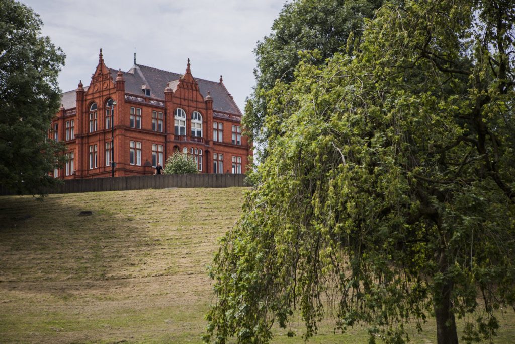 Taken from Peel Park, in the foreground  is green grass and trees covered in leaves. In the background you can see the back of a gorgeous red brick building from our campus.