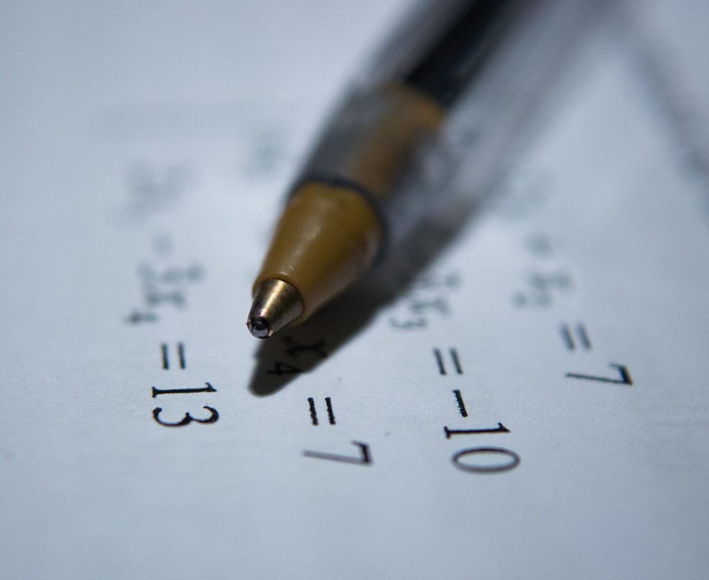An up close shot of a biro pen and some mathematical sums.