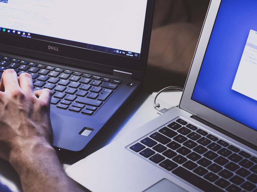 Up close shot of somebody working with two separate laptops.