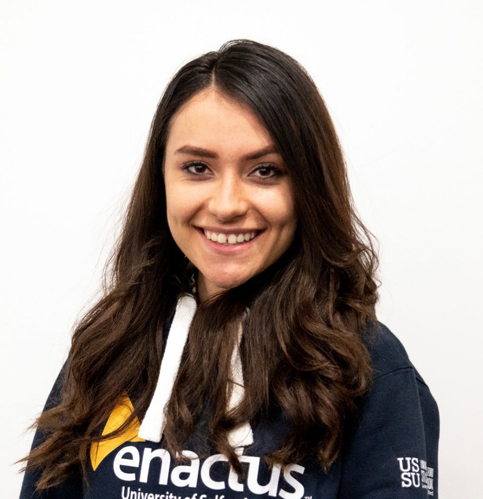 A headshot of Andreea herself. She is wearing one of the navy Enactus logo hoodies and her brown hair is down in curls. She is smiling.