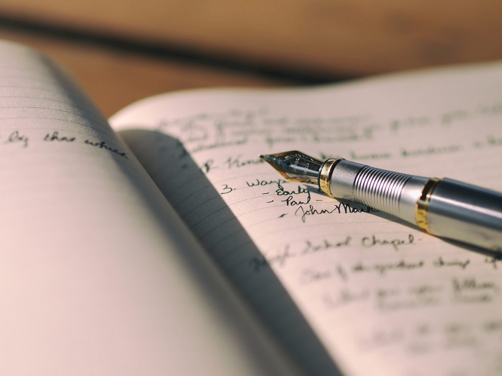 A gold and silver fountain pen sits on top of a lined notebook that has a lot of writing in it. 