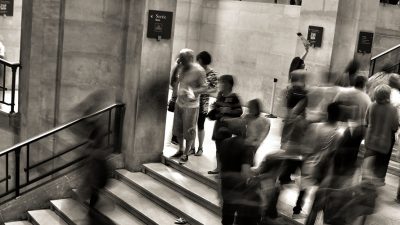 Edited in dark sepia/black and white this is a photo taken with adjusted shutter speed. It shows people and crowds moving throughout a station, people's movement is blurred.