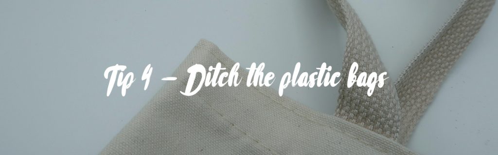 Image source is Photo by Mel Poole on Unsplash. In the background you can see a shot of the upper corner and handle of a beige cotton tote bag. The foreground has white text that reads 'Tip 4 - Ditch the plastic bags'.