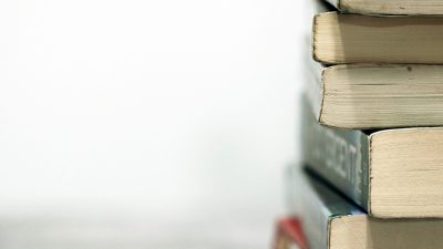 On a white background, a stack of books sits on a desk, the bottom ends of the books facing the camera.